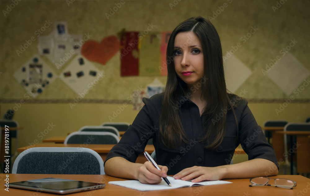 Φωτογραφία Happy student girl sits at a desk in the class room writes in a notebook and prepares to pass exam