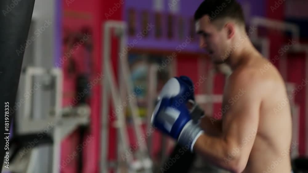 A professional boxer is conducting strikes on the punching bag with Boxing gloves bare-chested. A vertical camera movement in close-up. Pan. The legs of the boxer. A professional boxer is conducting strikes on the punching bag with Boxing gloves bare-chested. A vertical camera movement in close-up. Pan. The legs of the boxer.