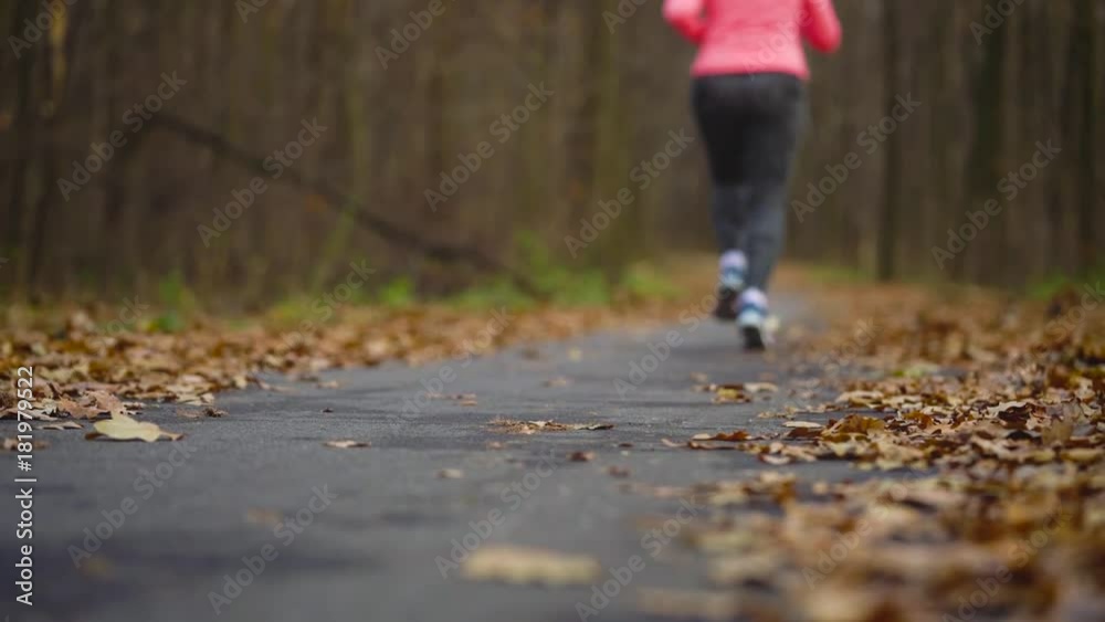 Close up of woman with headphones and smartphone running through an autumn forest at sunset. Slow motion Close up of woman with headphones and smartphone running through an autumn forest at sunset. Slow motion