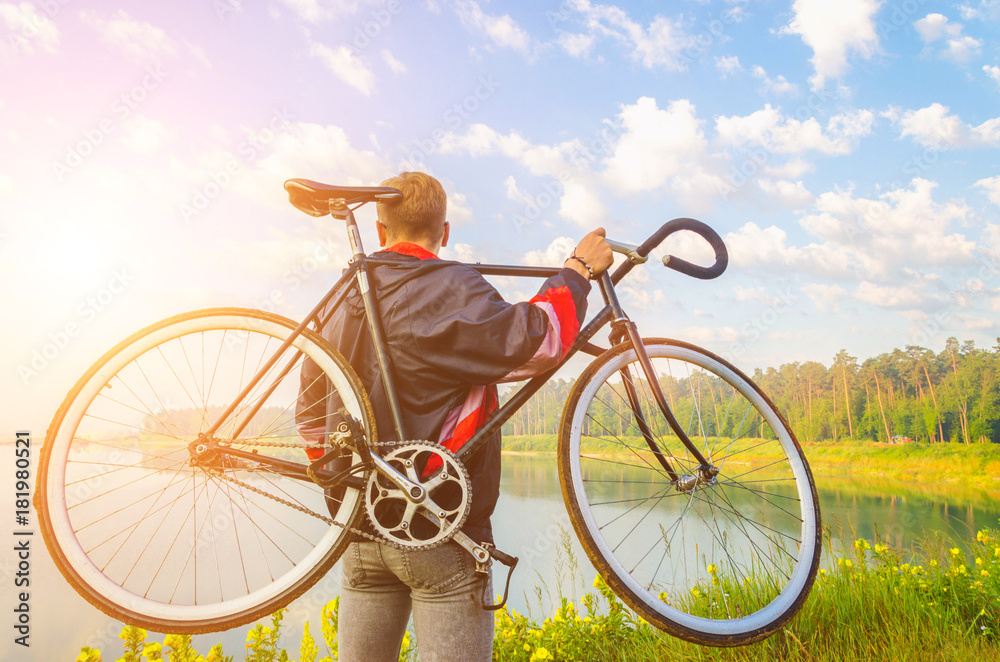 Fototapeta premium man stand with bicycle in hands on the hill and looking at the lake with azure water. sunrise