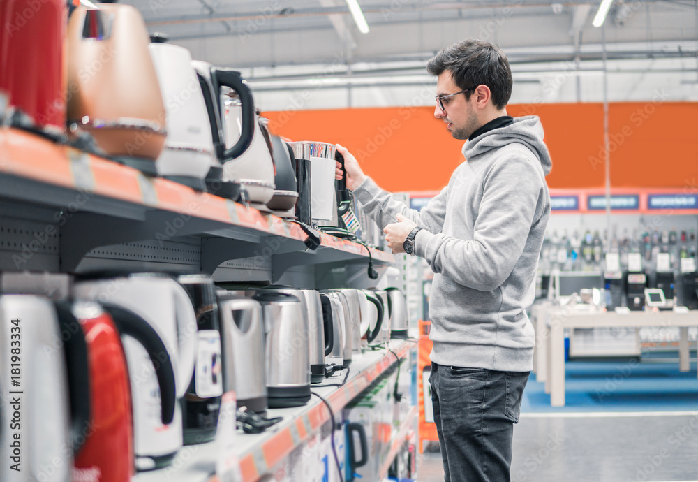 Smart young customer chooses a kettle in supermarket mall, difficult decision. Various choice Smart young customer chooses a kettle in supermarket mall, difficult decision. Various choice