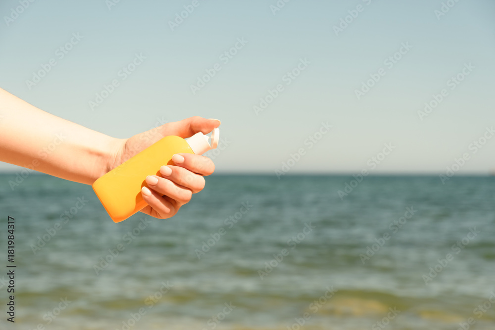 Female hand holds the bottle against a sandy beach and sea in bright Sunny day from left side of frame more yellow