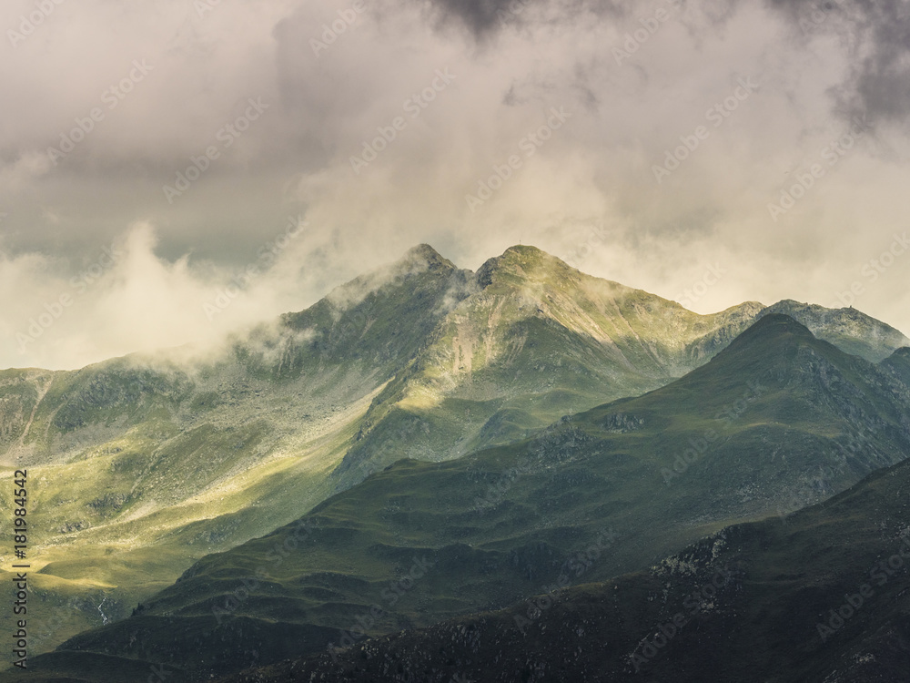 Green mountains in sun and shadow, twin peaks, covered in clouds, alps, Southtirol