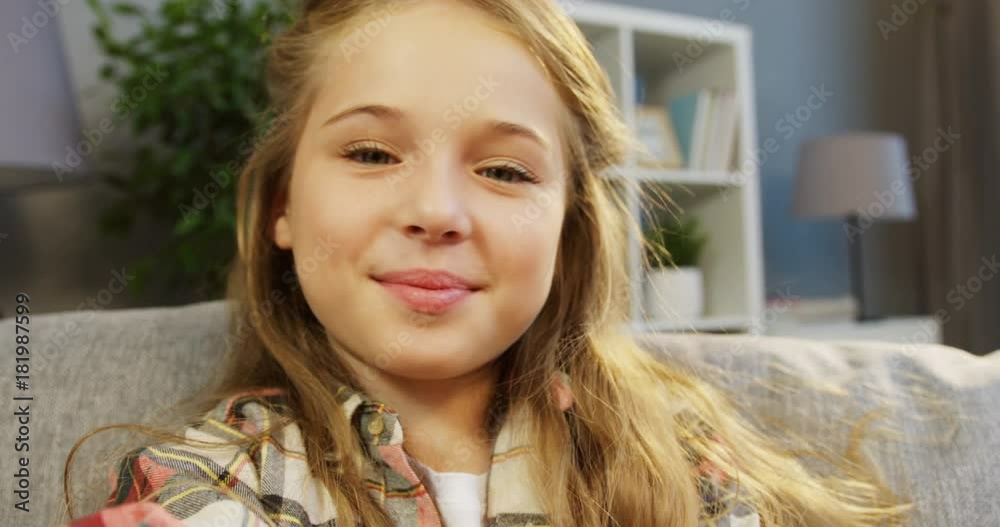 Close up of a cute 10 years old girl making selfies and smiling to the camera in the living room. POV. Indoor. Portrait