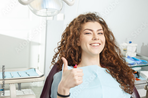Young female patient visiting dentist office.Beautiful smiling woman with healthy straight white teeth sitting at dental chair and making thumbs up.Dental clinic.Stomatology