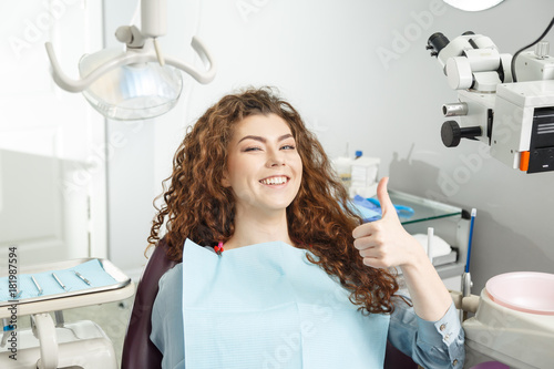 Young female patient visiting dentist office.Beautiful smiling woman with healthy straight white teeth sitting at dental chair and making thumbs up.Dental clinic.Stomatology