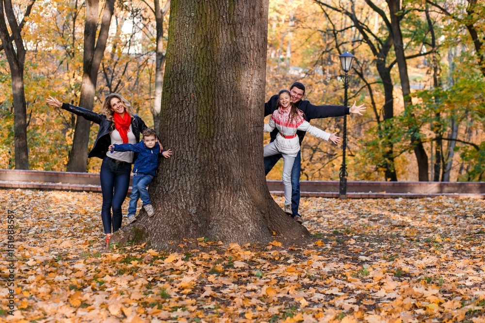 Fototapeta premium A happy family having fun in the park in autumn walking and hugging. Family, love, happiness concept. Family of four with mother father sister and a little cute brother