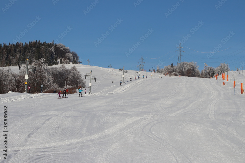 Ski slope with silhouettes of people in the distance on a beautiful snowy day