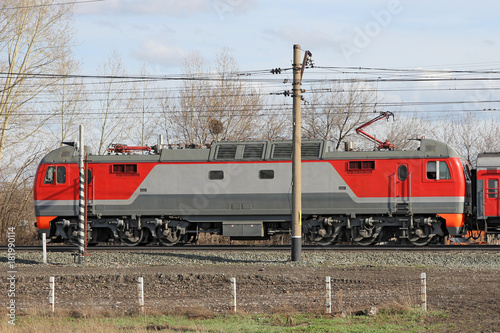 Red locomotive on electricity coming by rail.