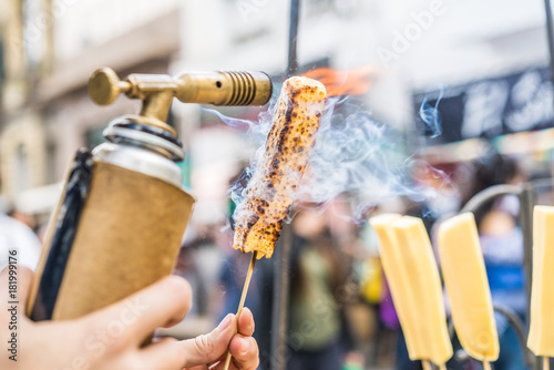 A chef grilling cheese with a kitchen gas torch at a food market