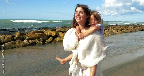 Mother walking on beach holding little daughter on the back singing