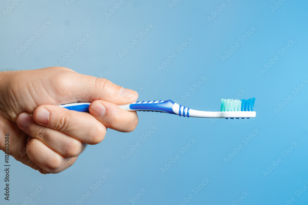 Blue toothbrush close-up in hand on blue background. The hygiene of the oral cavity. Blue toothbrush close-up in hand on blue background. The hygiene of the oral cavity.