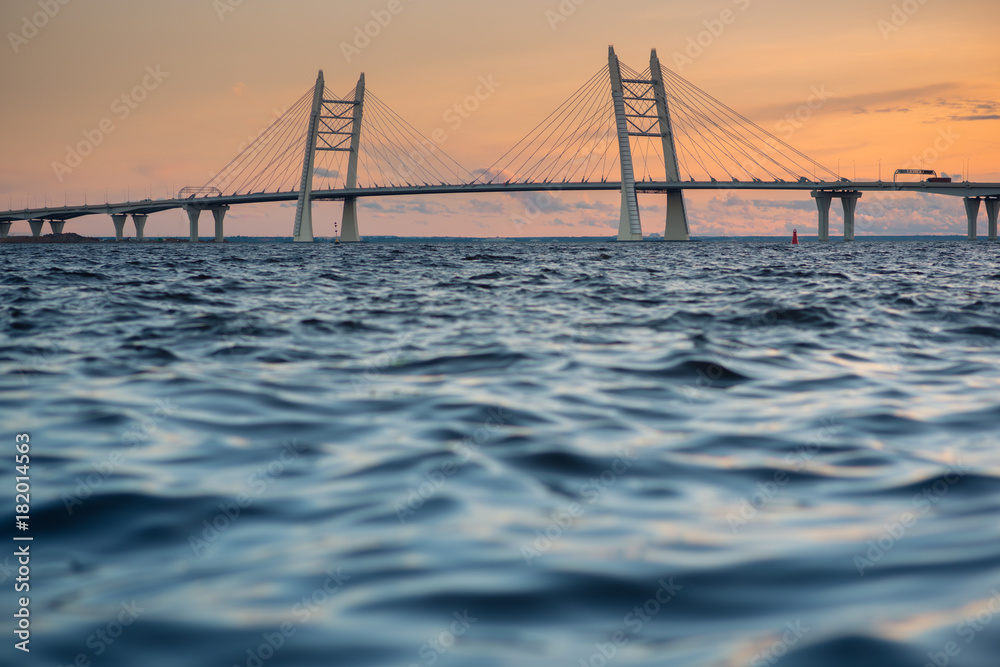 Cable-stayed bridge, at sunset, above the Ship's Channel of Saint Petersburg. A part of the Western Rapid Diameter. The water of the Gulf of Finland in the foreground.