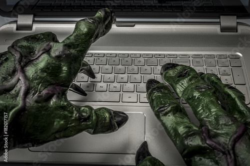 Cyber bullying, online fraud, computer virus or internet trolls concept with the hands of a troll typing on the keyboard of a laptop computer photo