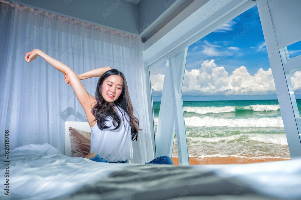 Beautiful woman stretch herself out on the couch in the morning in white bedroom with the sea view