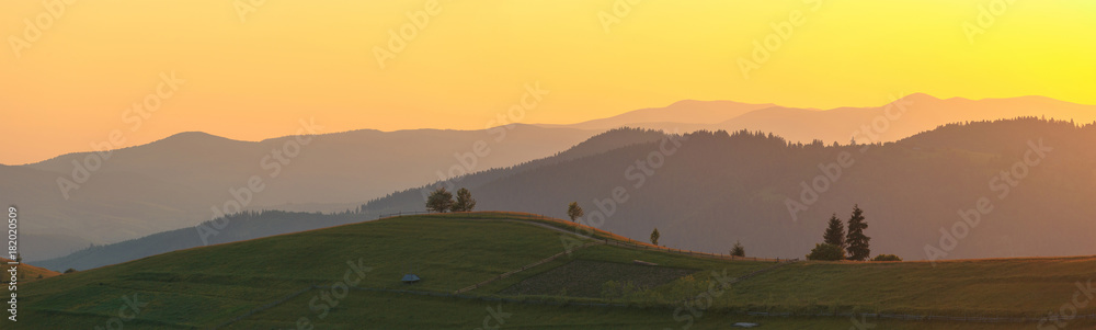 Obraz premium Wide panorama. Rural mountain landscape hills in scenic sunset light.