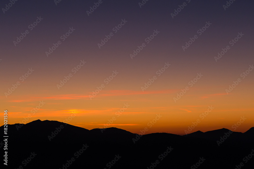A silhouette of a mountain peak at sunset, under a big sky with beautiful tones and colors
