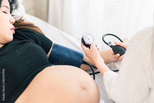 Female Obstetrician doctor  measuring blood pressure of the pregnant woman in the hospital. Pregnancy-induced Hypertension concept.