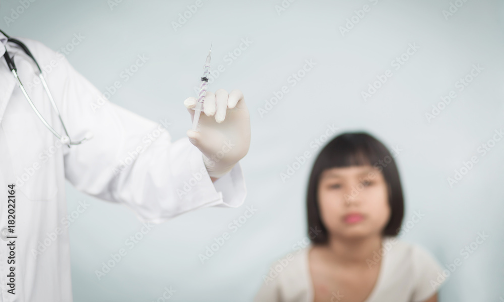Doctor holding a syringe with a liquid inside next to a girl arm. Blurred background of a girl. Doctor holding a syringe with a liquid inside next to a girl arm. Blurred background of a girl.