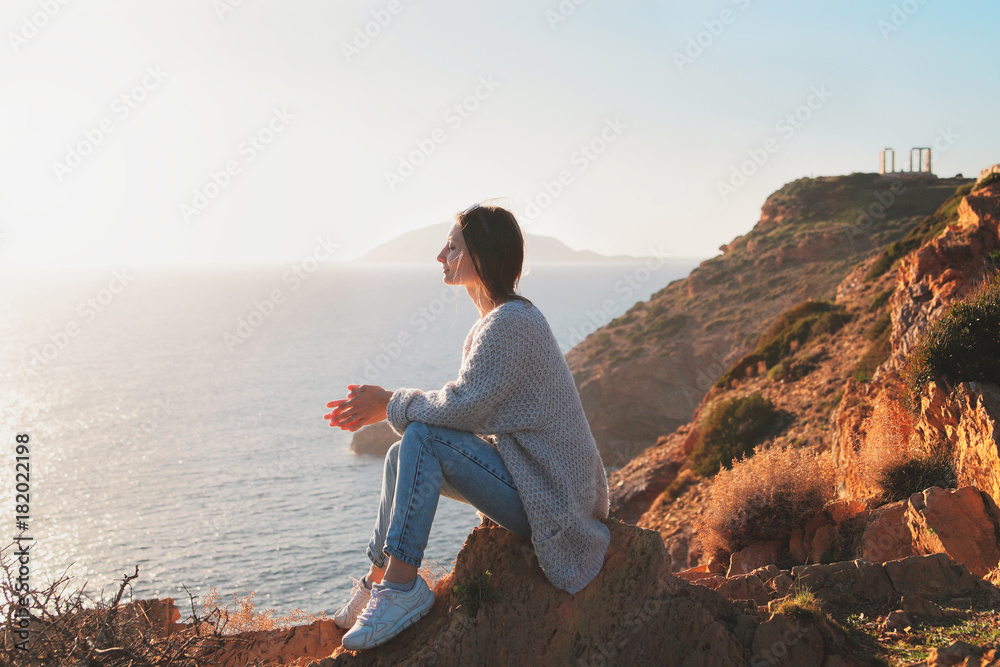 Traveler young woman sits on a cliff of cape Sounion and enjoys the moment.