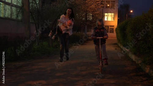 Girl on a Kick Scooter at Night Lights, Family Walking. 4K UltraHD video.