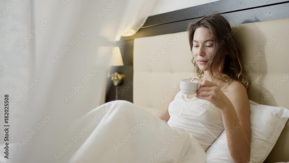 Woman using tablet pc on bed while drinking coffee Woman using tablet pc on bed while drinking coffee