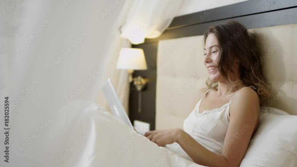Attractive woman using tablet pc on bed while tossing up a green apple Attractive woman using tablet pc on bed while tossing up a green apple