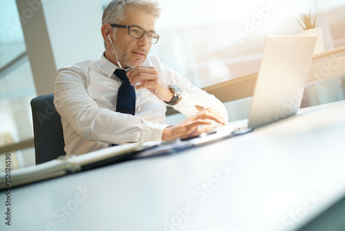 Businessman in office working on laptop and using earphones