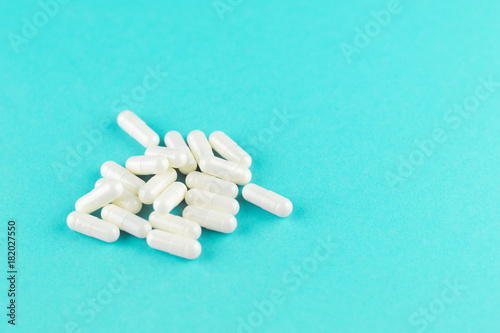 Close up white capsules on turquoise background with copy space. Focus on foreground, soft bokeh. Pharmacy drugstore concept