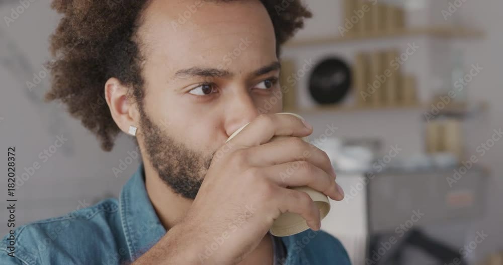 Portrait of african student drinking morning cappucino in bright cafe using paper disposable cup. Happy caffeine lovers and addicts