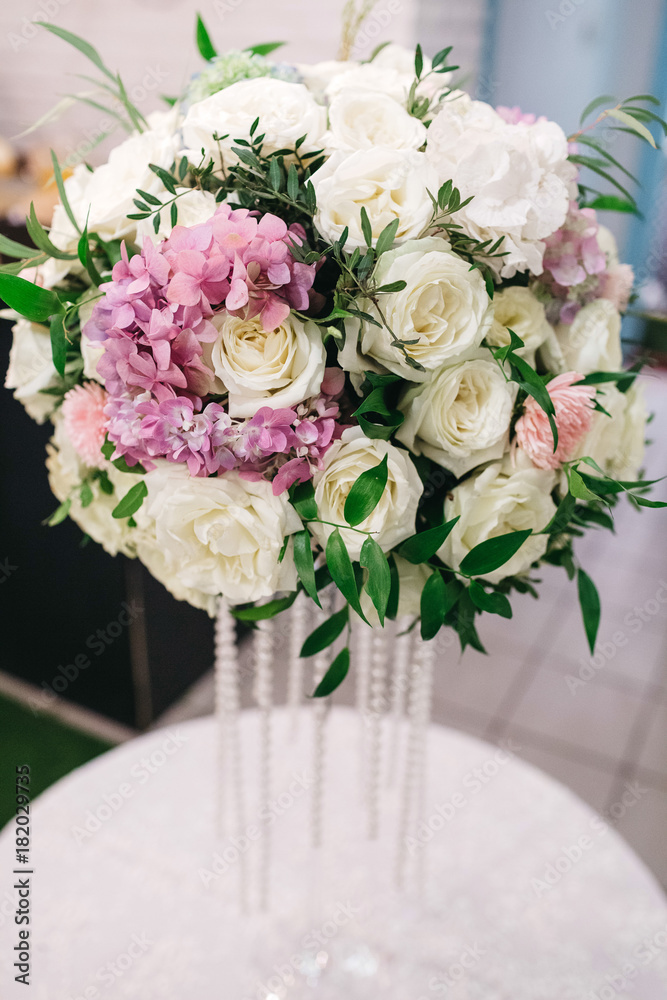 Obraz premium Centerpiece made of stunning white roses and pink hydrangeas stands on a little round dinner table