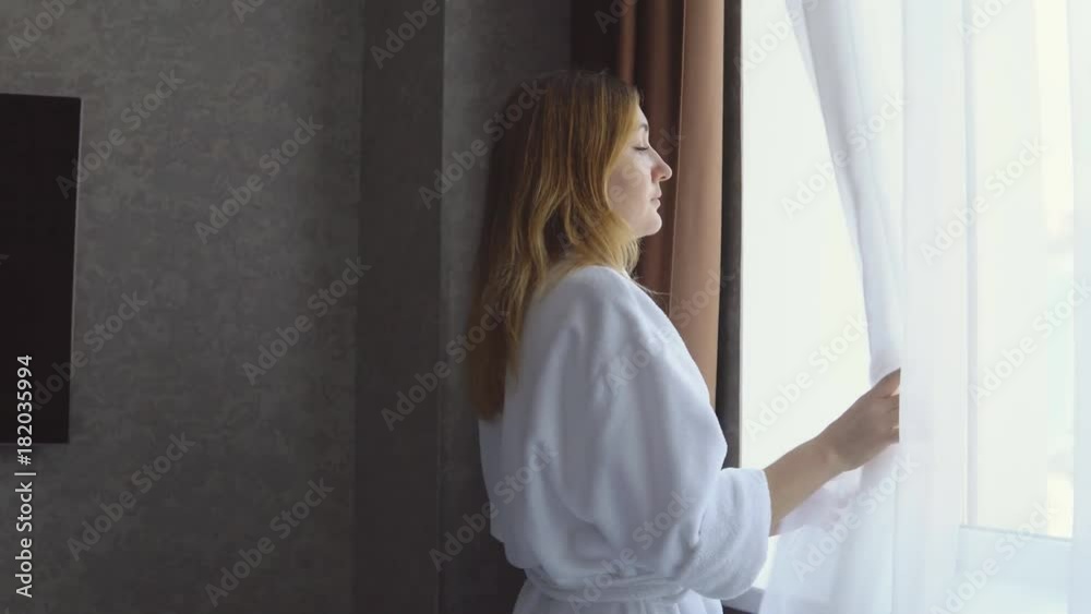Disturbing news. Young woman in white coat looks out the window and is horrified to see an emergency on the street Disturbing news. Young woman in white coat looks out the window and is horrified to see an emergency on the street