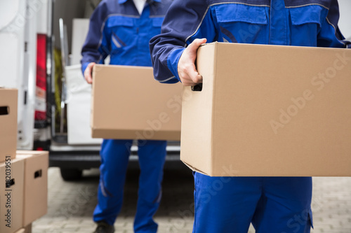 Close-up Of Two Movers Carrying Cardboard Box photo