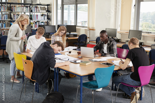 Busy College Library With Teacher Helping Students At Table