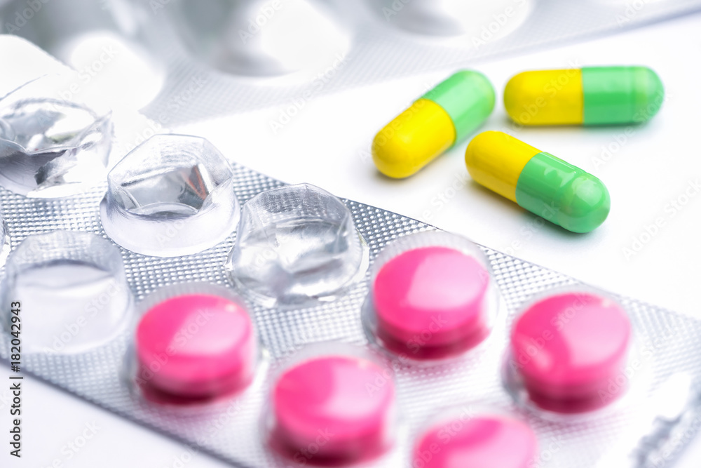 Yellow and green capsule with used magenta tablets, medical pills in silver foil pack on white background.