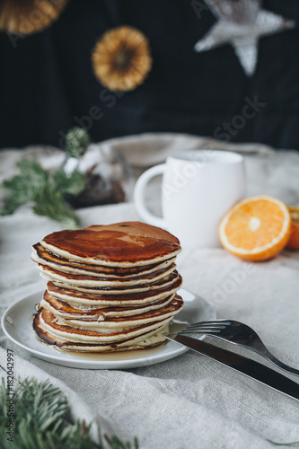 A still life of breakfast scene, that includes traditional american pancakes topped with maple syrop and sugar powder, a cup of black coffee and oranges