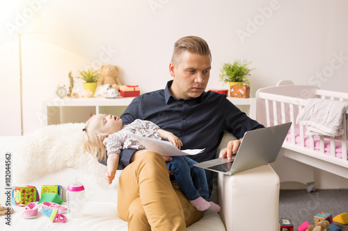 Busy father working on computer while holding sleeping baby photo