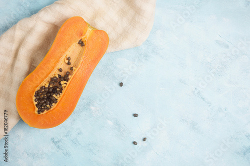 Half of colorful orange papaya fruit on kitchen tissue on blue and white table. Healthy vegetarian food concept. Detox