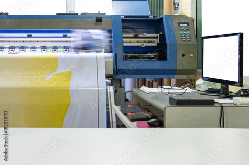 Large inkjet printer working on vinyl banner with computer screen