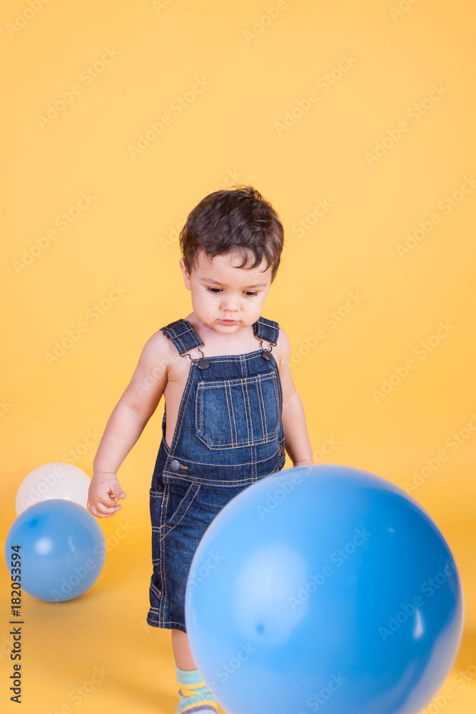 dreaming toddler in denim overalls on a yellow background with multi-colored balloons dreaming toddler in denim overalls on a yellow background with multi-colored balloons