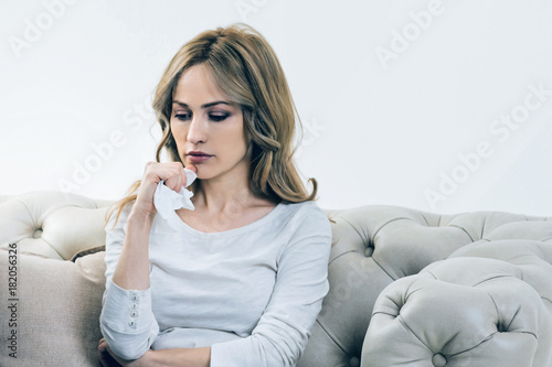 Personal problems. Unhappy depressed young woman holding a paper tissue and thinking about her problems while sitting on the sofa