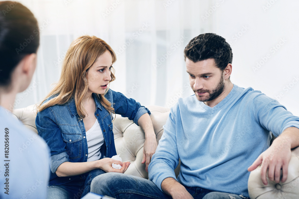 Discussion of problems. Unhappy sad young woman looking at her husband and talking to him while having a therapeutic session Discussion of problems. Unhappy sad young woman looking at her husband and talking to him while having a therapeutic session