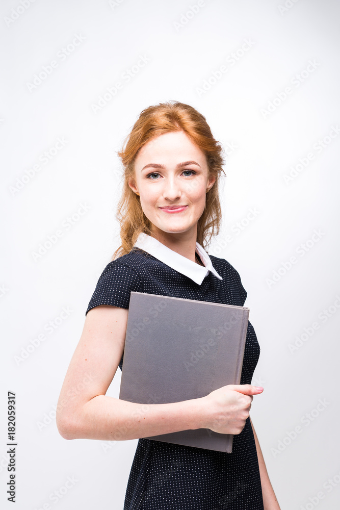Beautiful girl with red hair and gray book in hands dressed in black dress on white isolated background Beautiful girl with red hair and gray book in hands dressed in black dress on white isolated background