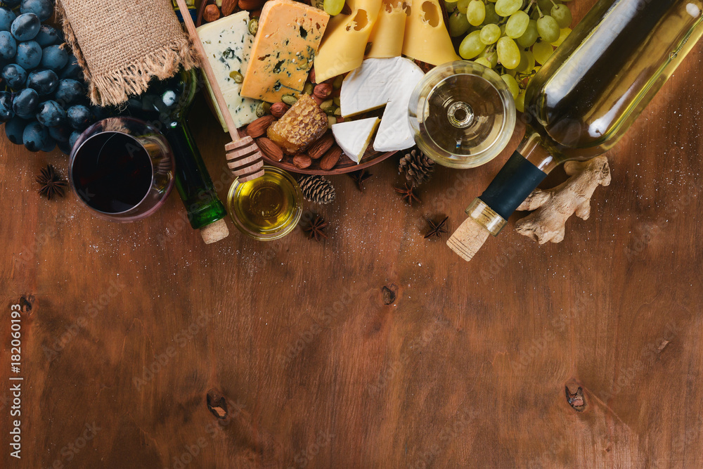 Fototapeta premium A bottle of wine, and a large assortment of cheeses, honey, nuts and spices, on a wooden table. Top view. Free space for text.