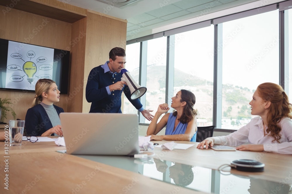 Angry businessman using megaphone in conference room