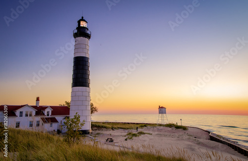 Michigan Lighthouse Coastal Sunset Background. Illuminated beacon of the Big Sable Lighthouse on the sandy coast of Lake Michigan at sunset. Ludington State Park in Ludington, Michigan.