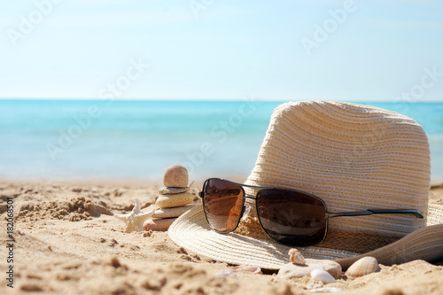 Pyramid of stones to the left of the hat with sunglasses on the sand against the blue sea