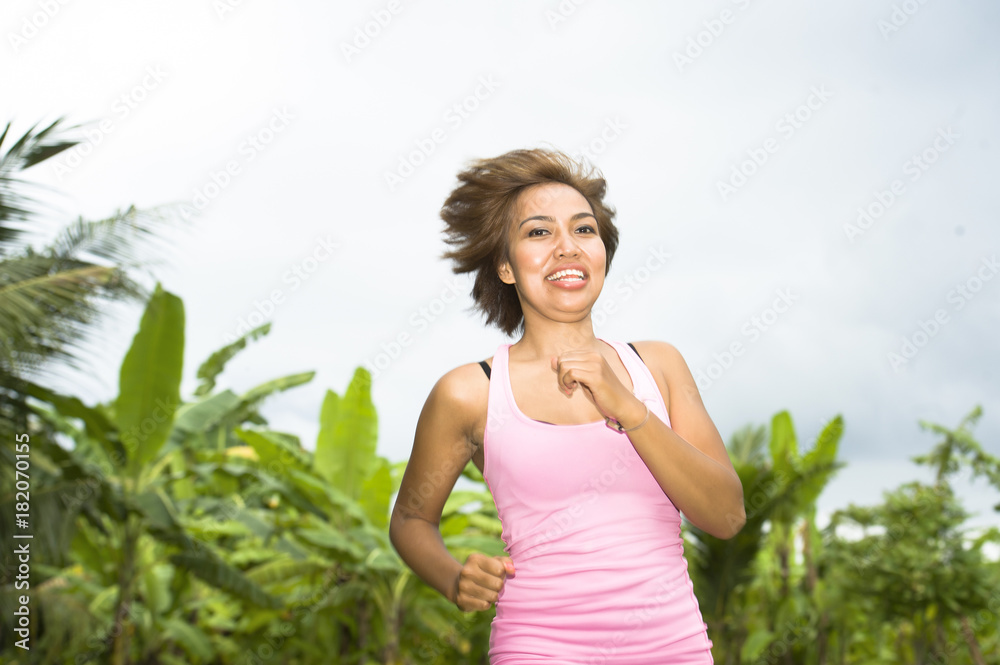 young attractive Asian sport runner woman running in the jungle smiling happy in training workout on herb with palm trees on the background young attractive Asian sport runner woman running in the jungle smiling happy in training workout on herb with palm trees on the background