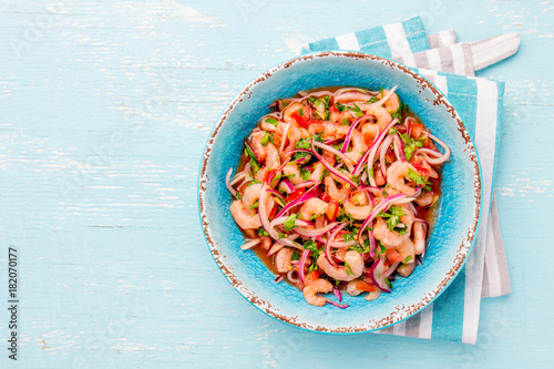 Ecuadorian shrimps ceviche sebiche with tomatoes in blue bowl, wooden blue background. Traditional ecuadorian colombian or mexican dish. photo