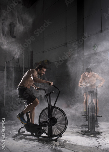 Muscular men cycling in a gym